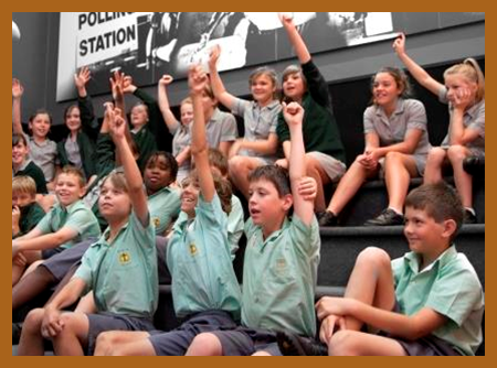 A group of children, hands raised, participating in a class discussion.