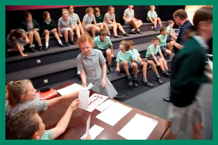 A girl is handed ballot papers by two students, in front of a class group in the theatrette.