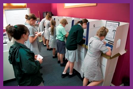 A group of students queuing and voting at voting screens.
